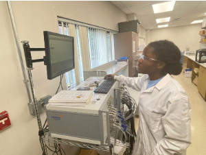 female student researcher in front of a monitor in a white lab coat conducting research on clean energy